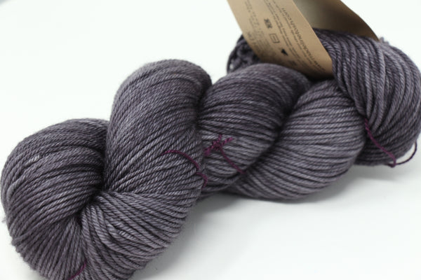 Madelinetosh Tosh DK yarn in a soft grey color, showing the skein with a subtle textured background.
