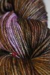 Madelinetosh Tosh DK yarn in a warm, rich color, displayed in a close-up shot showcasing the soft wool texture and branding.